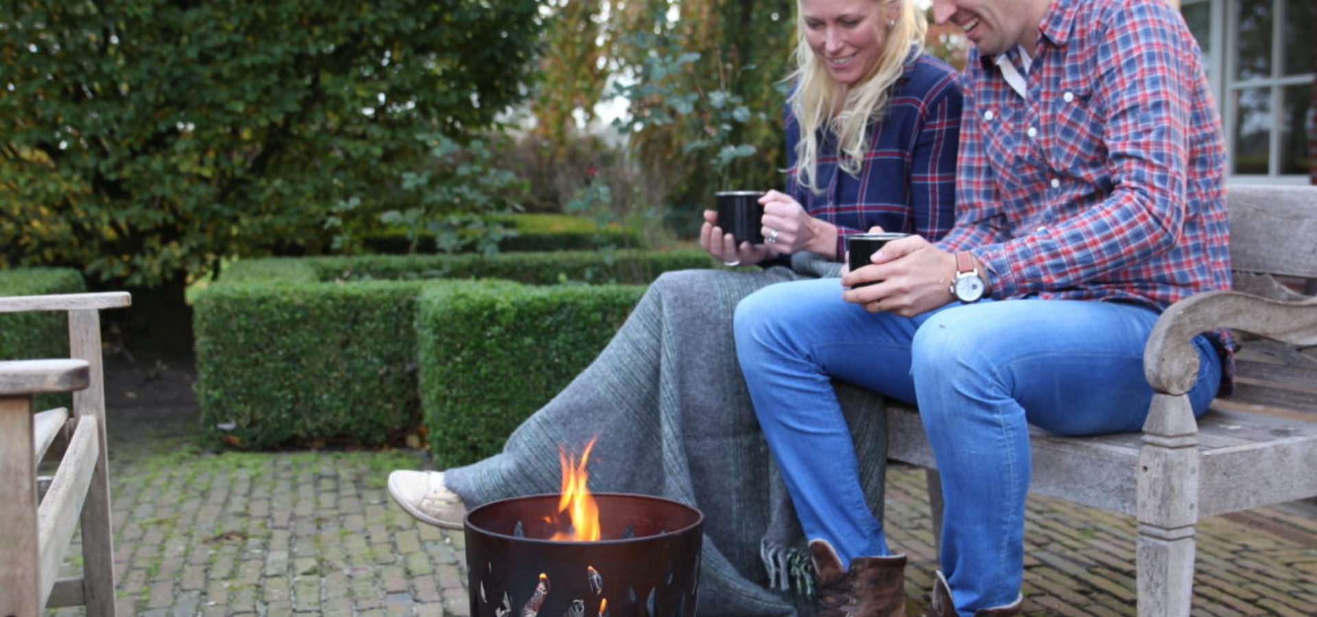 A man and a woman sat next to a lit metal fire basket