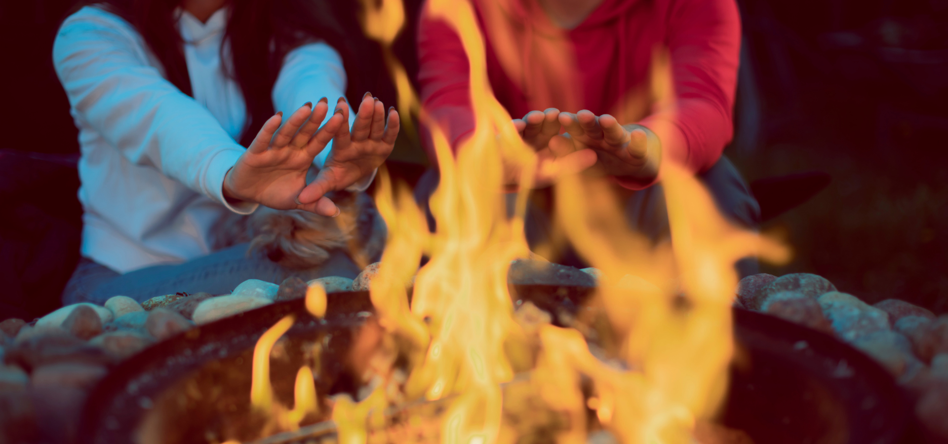 A man and a woman warming their hands on a fire