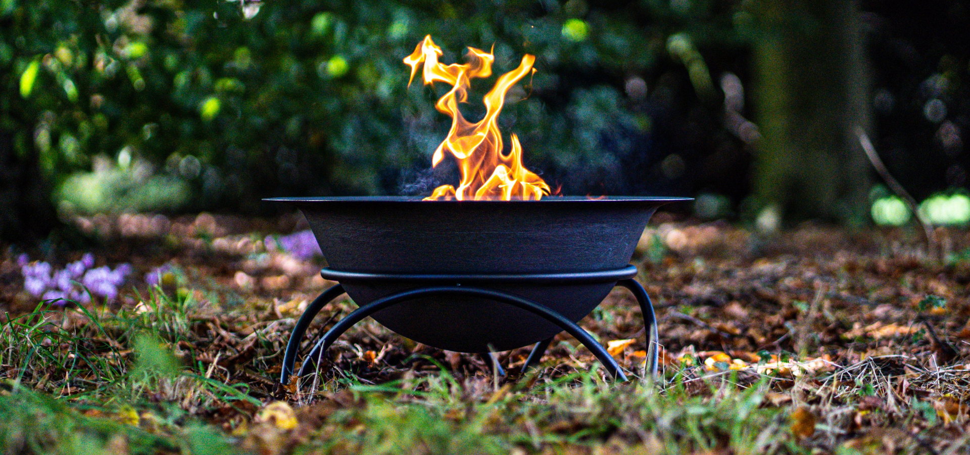 A lit Tintagel fire pit sat in a woodland area