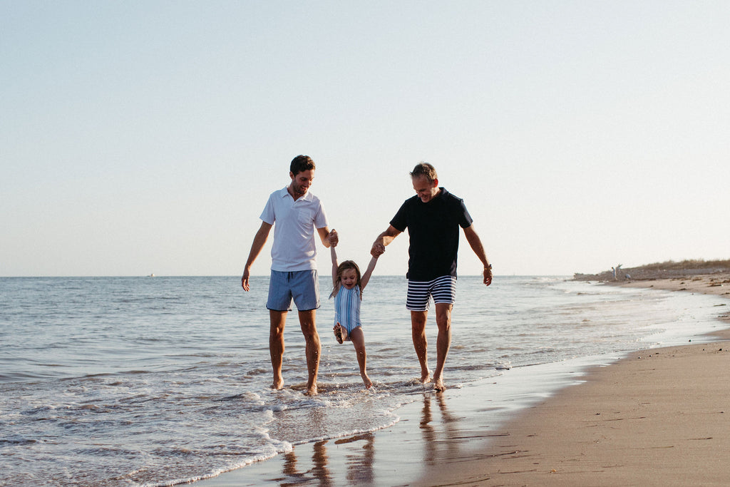 two dads on the beach with their daughter 