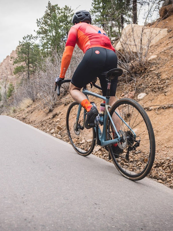 Cyclist wearing Summit Raptor bibs climbing uphill out of the saddle