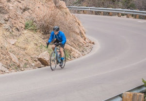 Male cyclist riding downhill waering a Divide Wind Jacket