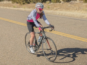 Woman cyclist riding on the road while wearing the Divide Wind Jacket
