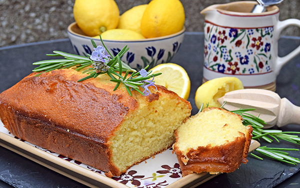 Nicholas Mosse lemon drizzle cake with rosemary on rectangular plate Clematis, with lemons in Blue Blooms bowl, wild flower meadow cylinder jug in background