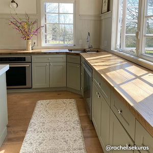 Emile latte neutral floral print standing mat shown in size 30x108 in a sage green kitchen inbetween the counter and island