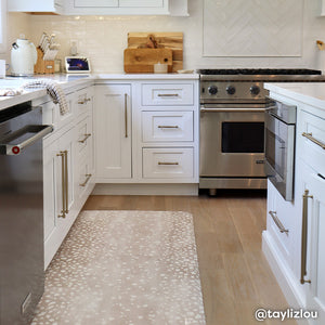 Fawn brown neutral animal print standing mat shown in white kitchen with in size 30x108. @taylizlou written in the lower right hand corner.