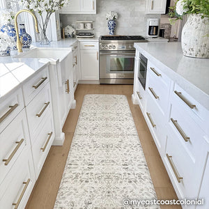 Emile latte neutral floral print standing mat shown in size 30x108 in a white kitchen inbetween the counter and island