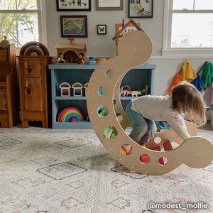 Neutral boho print baby play mat shown in play room with toddler playing on wooden rocker. @modest_mollie written in bottom right hand corner.