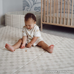 Checker almond neutral geometric print tumbling mat shown in a nursery with toddler boy sitting on the mat eating a snack 