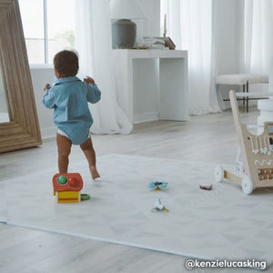 Gallery terrazzo cream geometric print play mat shown in play room with with various toys and baby boy walking on the mat. @kenzielucasking written in bottom right hand corner.