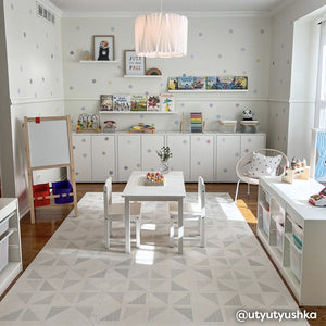 Gallery terrazzo cream geometric print play mat shown in play room with a craft table in the middle next to an easel. Walls and built in cabinets on the back wall painted with polka dots. @utyutyushka written in bottom right hand corner. 