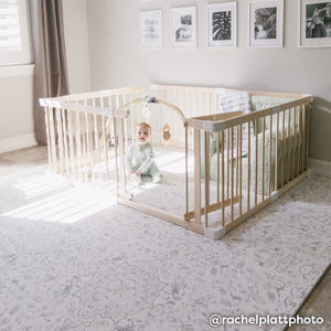 Emile latte neutral floral print play mat shown in room with baby playing in wooden playpen on top of the mat