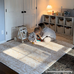 Ula amber brown boho print play mat shown in kaplay room with mom and baby playing on the mat and mom kissing baby on the head. @sammieadamsblog written in bottom right hand corner.