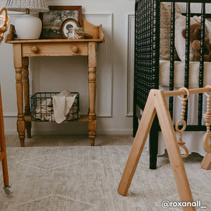 Ula gray boho print play mat shon in nursery with wooden play set next to black wooden crib. @roxanal_ written in bottom right hand corner.