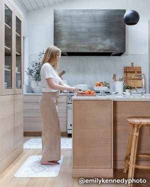 Nama Standing Mat in Ula Oat neutral boho print. Anti-fatigue kitchen mat in two sizes shown in kitchen with woman making food on the island.