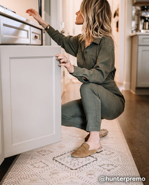 Nama Standing Mat in Ula Oat neutral boho print. Anti-fatigue kitchen mat shown in kitchen with woman bending down to open a cabinet.