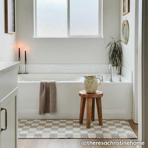 Harbor grey beige and gray checker print bath mat in front of a bathtub with stool and pitcher on top