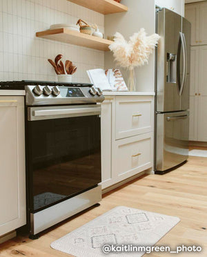 Nama Standing Mat in Ula Oat neutral boho print. Anti-fatigue kitchen mat shown in kitchen in front of stove.