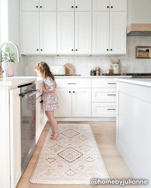 Nama Standing Mat in Ula Oat neutral boho print. Anti-fatigue kitchen mat shown in kitchen between island and counter with little girl standing at the sink.