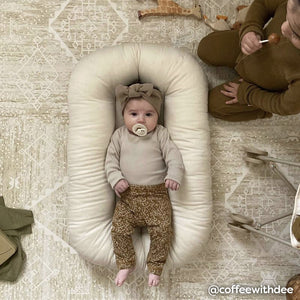 Ula straw neutral tan boho print play mat shown with baby laying in lounger on the mat with older sibling sitting next to them eating a sucker. @coffeewithdee written in the bottom right hand corner.
