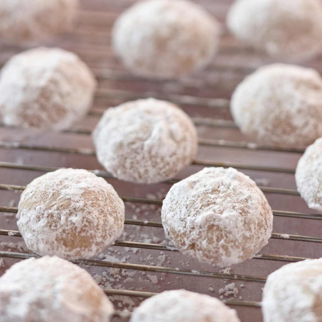 Bite sized Danish wedding cookies covered in powdered sugar on a cooling rack