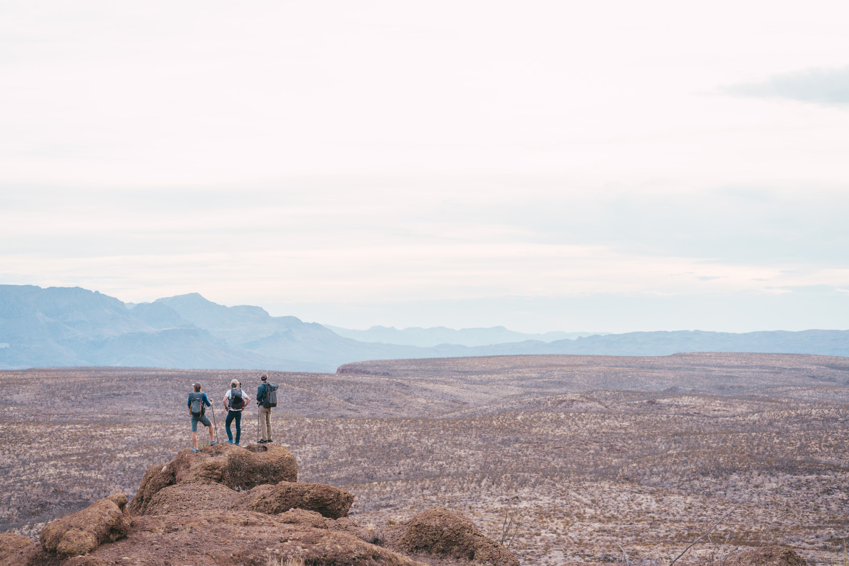 Three people standing on the edge of a desert cliff