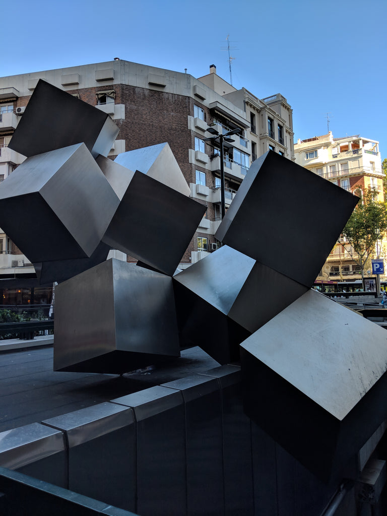 Eight large metal cubes in front of a building and blue sky