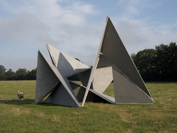 A massive metal geometric sculpture stands in a vast field.