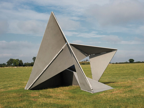 A massive metal geometric sculpture stands in a vast field.
