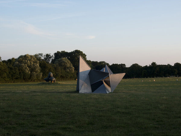 A massive metal geometric sculpture stands in a vast field at dusk.