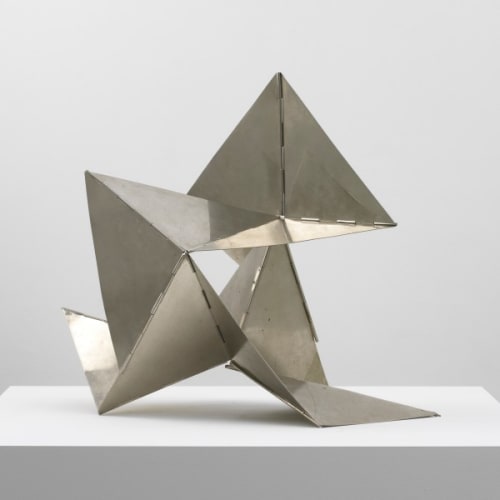 A metal triangle sculpture on a white surface, showcasing geometric elegance and modern artistry.