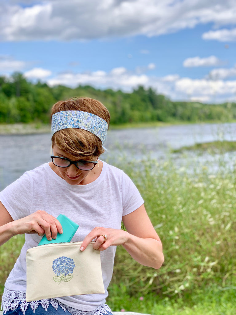 girl taking glasses case out of embroidered hydrangea clutch bag