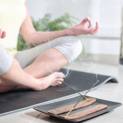 Woman practicing yoga in front of gently smoking incense sticks in simple wooden incense holders