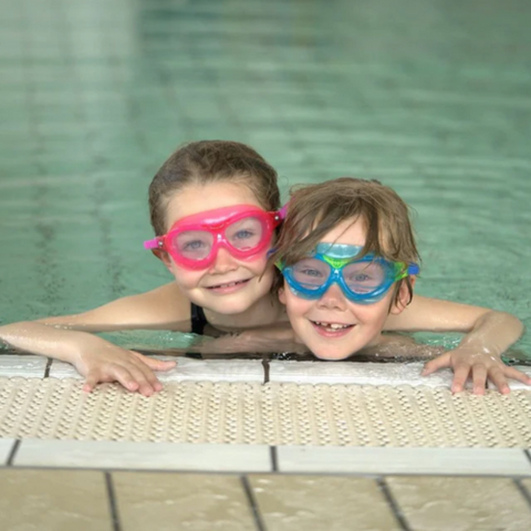 Billedet viser 2 børn i en svømmehal, som udstråler glæde og nyder at sit ophold i vandet.