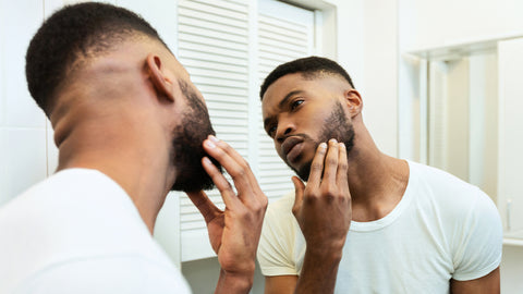 Man looking into mirror touching and reflecting on the growth of his beard