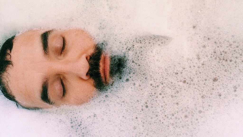 Bearded man about to use beard wash in a bath tub