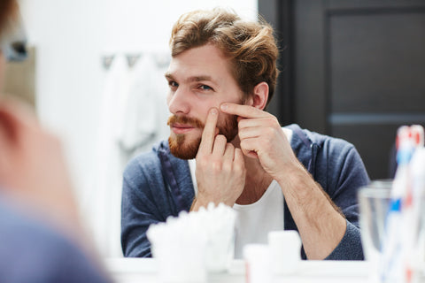 Man examining a blemish that could have been prevented by she butter in his beard