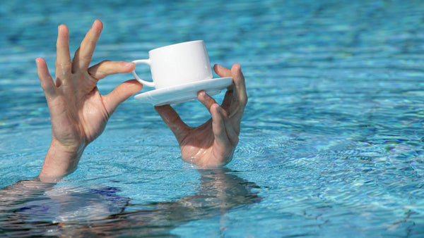 hand holding a cup of coffee in a swimming pool. 