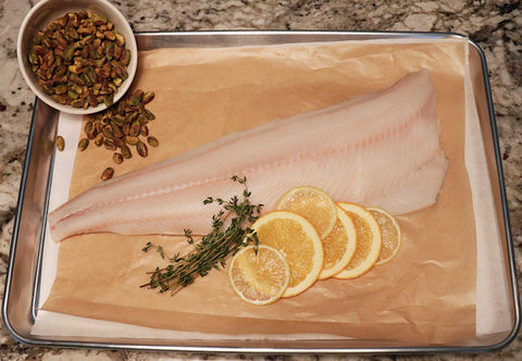 black cod on baking sheet with lemon and pistachio