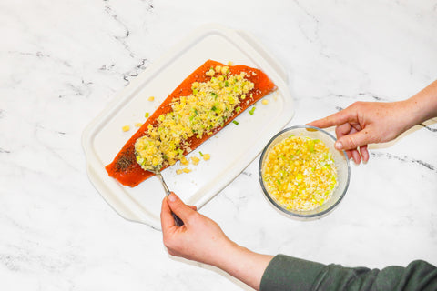 Salmon Fillet on a white dish while Chef Nicole spoons the pineapple leek mixture on top of the salmon