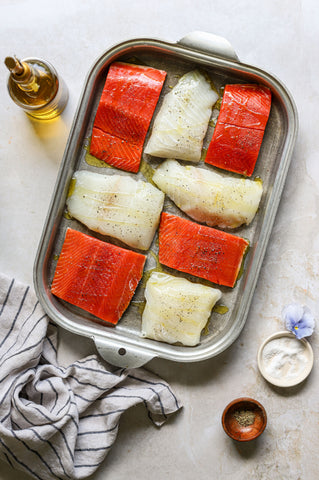 Red salmon and white fish seasoned with salt pepper and olive oil sit atop a backing dish in this recipe perfect for grilling 4th of July party food.