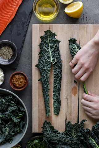 Marisa taking the stalk out of the kale on the wooden cutting board. Surrounded by multiple spices and ingredients