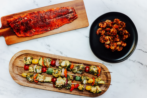 Grilled salmon fillet, shrimp, and cod skewers on a white marble table