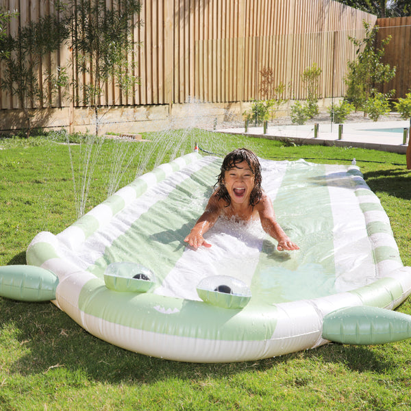 Image shows a child sliding down the Shark Tribe Slip and Slide while water splashes above