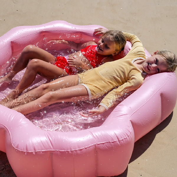 Image shows two children lying back in water in the Ocean Treasure Shell Shaped Pool