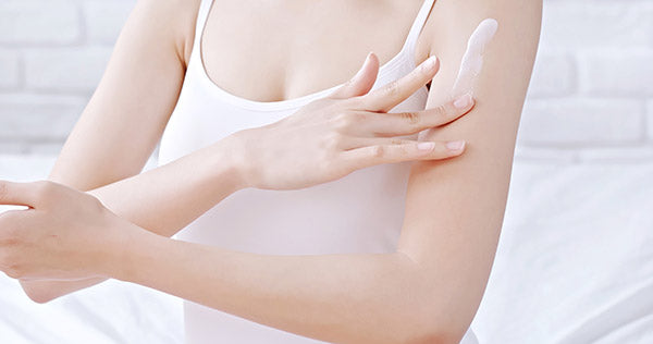 Woman applying skin cream to her arm.