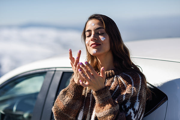 Young woman applying sunscreen on her face in snow landscape.