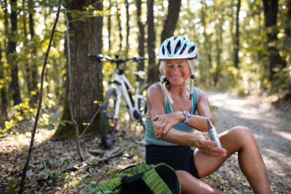 Happy woman biker sitting and applying sunscreen on her arm outdoors in forest.