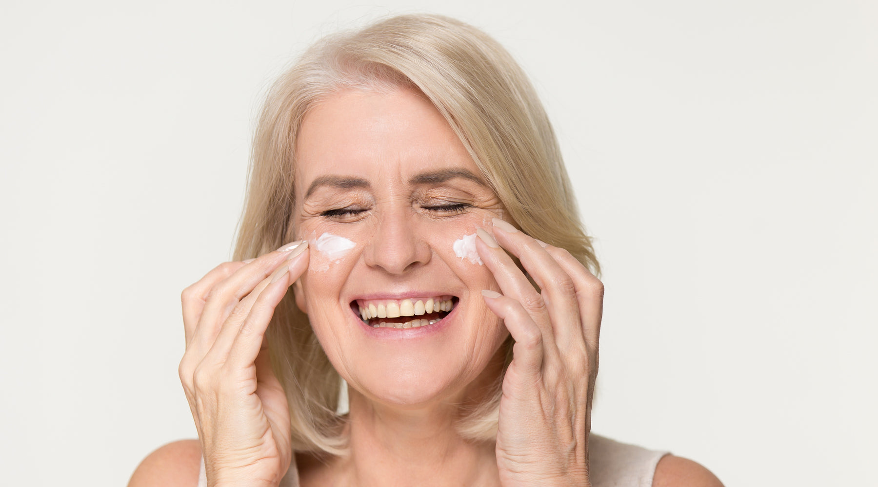 Laughing woman applying cream to her face 