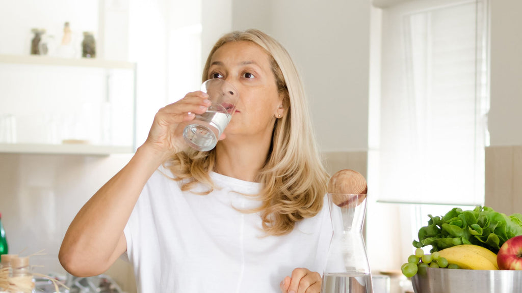 A middle aged woman drinking water in the kitchen to stay hydrated during winter.